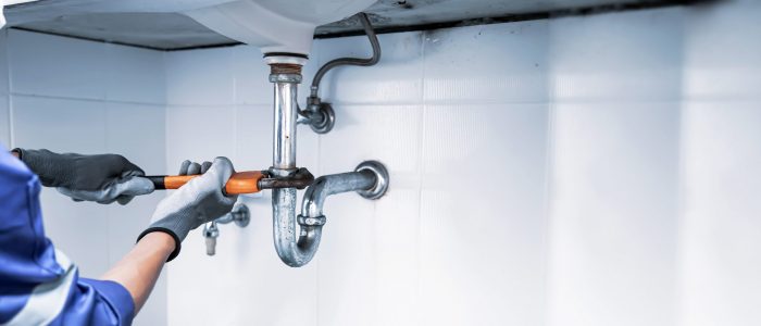 Technician plumber using a wrench to repair a water pipe under the sink. Concept of maintenance, fix water plumbing leaks, replace the kitchen sink drain, cleaning clogged pipes is dirty or rusty.